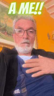 a man with glasses and a beard holds his hand to his chest in front of a sign that says a me