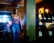 a woman in a pink top and blue jeans is walking through a room with a box that says ' moving ' on it