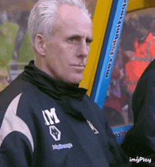 a man with gray hair is wearing a black jacket with the letter m on the front .