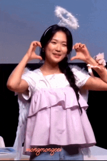 a woman wearing angel wings and a halo makes a heart with her hands