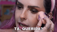 a woman with pink hair is applying makeup to her face with a sponge and says ta , querida ?