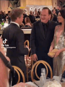 a man in a suit is talking to a woman in a dress at a dinner table .