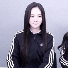 a woman wearing a black adidas jacket with white stripes on the sleeves