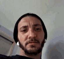 a man with a beard and ear buds is wearing a hat and making a funny face .