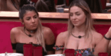 two women are sitting at a table with red cups and plates .