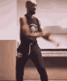 a man in a black tank top and black pants is dancing in a room .