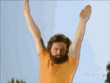 a man with a beard wearing a yellow shirt is raising his arms in the air ..