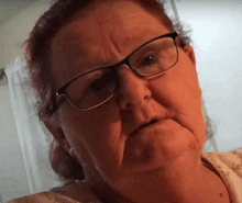 an older woman wearing glasses looks at the camera with a serious look on her face