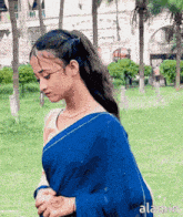 a woman in a blue saree is standing in a park and the word alamin is on the bottom