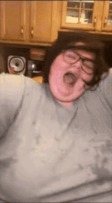 a man wearing glasses and a gray shirt is yawning