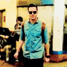 a man in a blue shirt and sunglasses is walking