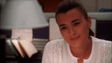 a woman in a white shirt looks at the camera with a lamp in the background