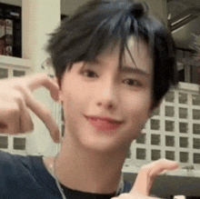 a young man with short black hair is making a heart shape with his fingers .