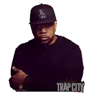 a man wearing a la hat stands in front of a poster for trap city