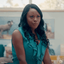 a woman in a blue top is making a funny face while sitting in front of a window .