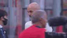 a bald man with a beard wearing a white shirt is standing in a room with other people .
