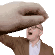 a man in a suit and glasses is being slapped in the face by a large hand .