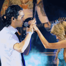 a man holding a woman 's hand in front of a microphone with the word mafia on the bottom right