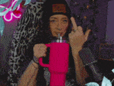a woman wearing a black hat that says this year is holding a pink mug and giving the middle finger