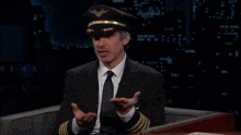 a man in a suit and tie is sitting in a chair wearing a pilot 's hat .