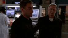 a man in a black suit stands next to another man in a black jacket