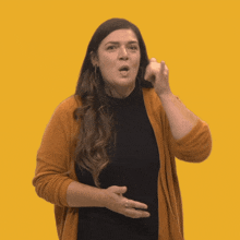 a woman wearing a black shirt and an orange sweater makes a gesture with her hands