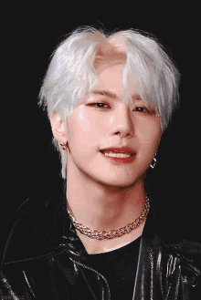 a young man with white hair and a gold chain around his neck is pointing at the camera
