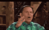 a man in a green plaid shirt is making a funny face with his mouth open .
