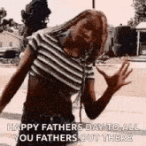 a woman in a striped crop top is standing on a sidewalk with her arms outstretched .
