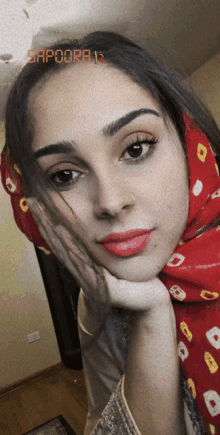 a woman with a red scarf around her head takes a selfie with sapoora 13 written on the bottom right