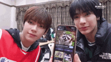 two young men are holding a phone with a raccoon on it