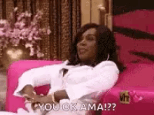 a woman is sitting on a pink couch and says `` you ok ama ! ''
