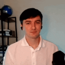a young man in a white shirt is standing in front of a microphone and smiling .