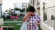 a man in a plaid shirt is covering his face with his hand while walking down a sidewalk in a park ..