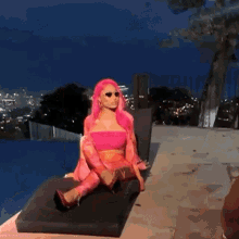 a woman with pink hair and sunglasses is sitting on a couch by a pool .