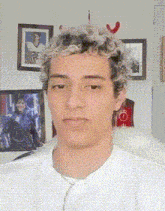 a young man wearing a white shirt is standing in front of a wall with pictures on it ..