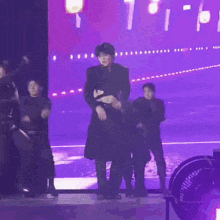 a man in a black coat is dancing on a stage with a group of people .