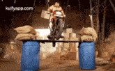 a police officer is riding a motorcycle over a bridge made of barrels .