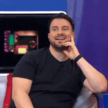 a man with a beard is smiling while sitting in front of a screen .