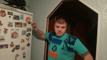 a man in a blue shirt with the letter n on it stands in front of a fridge