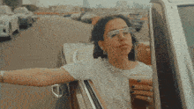 a woman wearing glasses and a white shirt is looking out of a car window