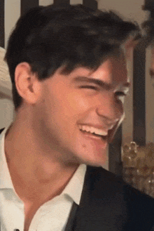 a man in a suit and white shirt is laughing with his mouth open .