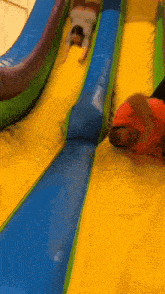 a woman is sliding down a slide with a man laying on the ground behind her