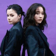 two women standing back to back with purple background
