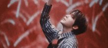 a man in a striped shirt is standing in front of a red wall with his arms in the air .