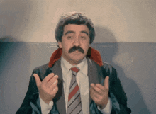 a man with a mustache is wearing a suit and tie with his hands outstretched