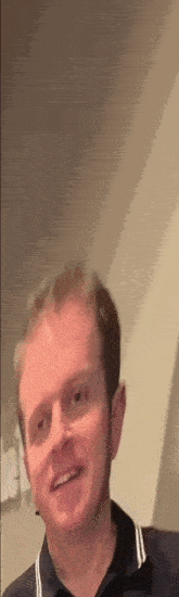 a man in a black shirt is smiling and looking at the camera in a room .