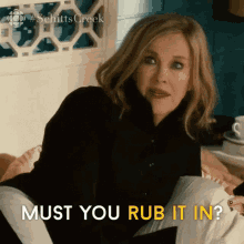 a woman is sitting on a bed with a pillow in her lap and the words `` must you rub it in '' .