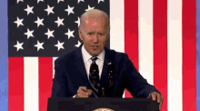 a man in a suit and tie is standing at a podium in front of an american flag giving a speech .