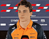 a young man wearing a mclaren shirt is standing in front of a microphone .